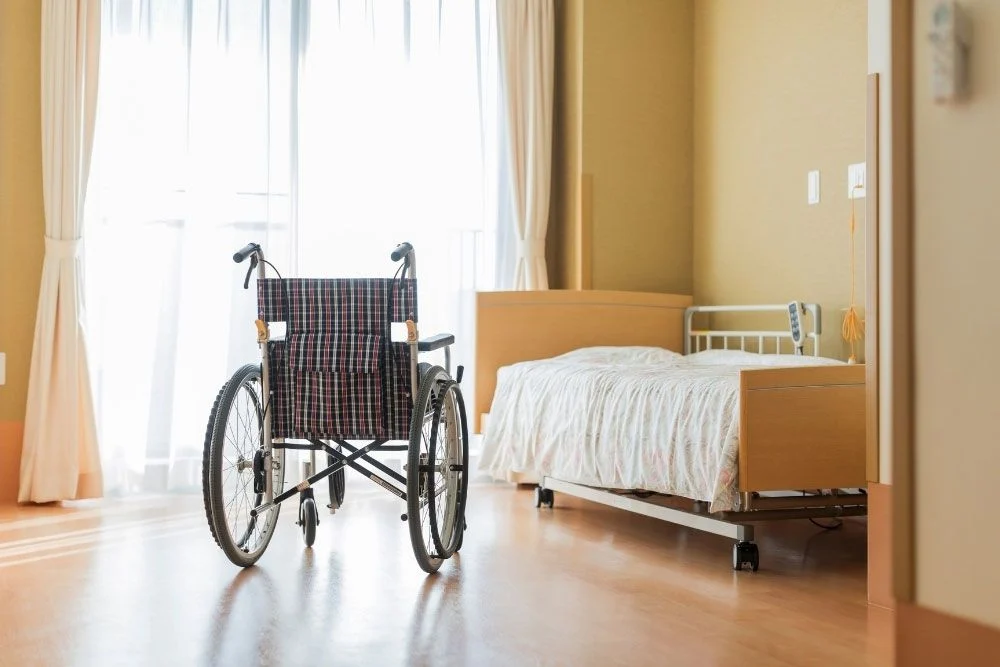 Empty wheelchair and bed in a nursing home room. Webster & Garino helps protect assets from nursing home costs.